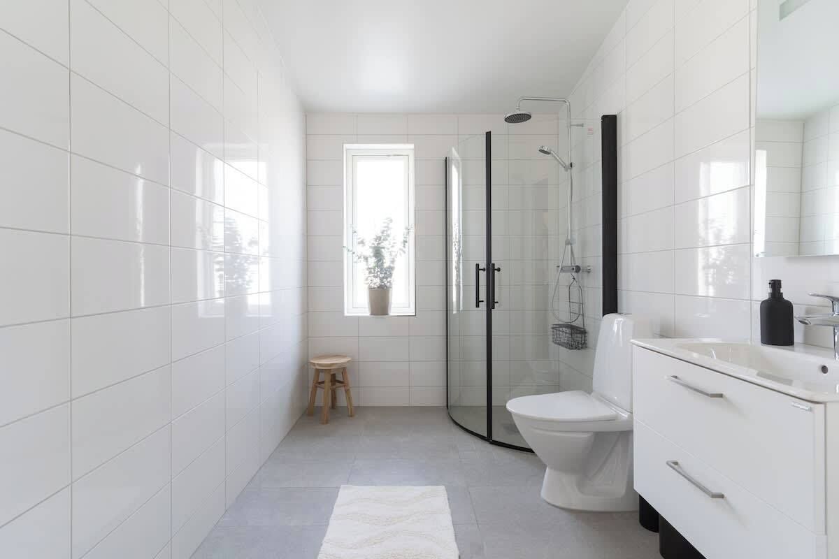 A modern bathroom with white tiles, a glass shower enclosure, a toilet, and a vanity with drawers.