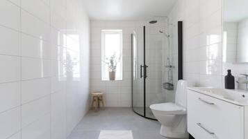 A modern bathroom with white tiles, a glass shower enclosure, a toilet, and a vanity with drawers.