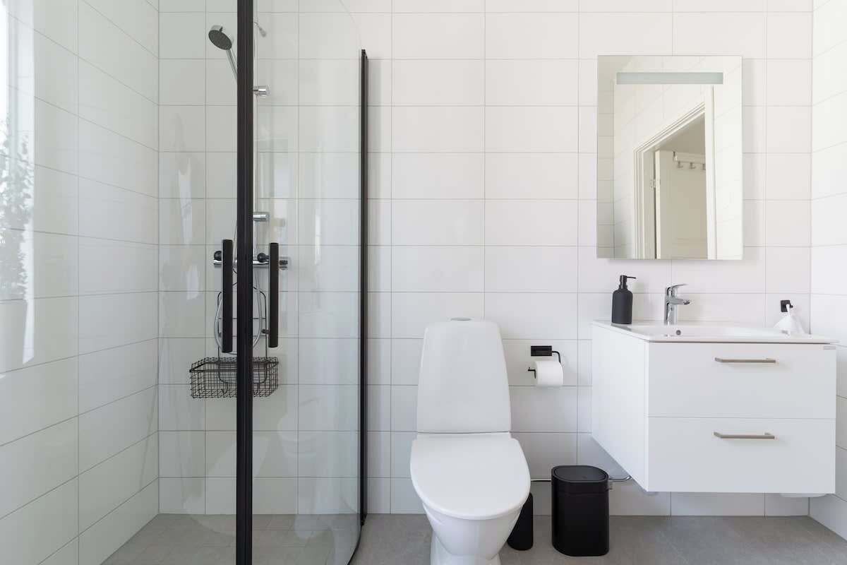 A modern bathroom with a glass shower enclosure, a toilet, a sink with a mirror, and a trash bin.