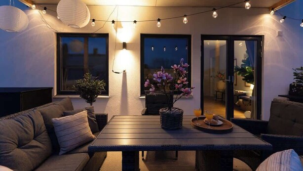 A cozy outdoor seating area with a wooden table, cushioned chairs, and string lights.