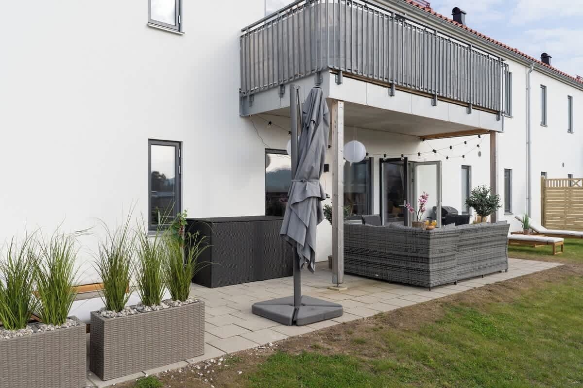 Ein modernes Haus mit Balkon, Sitzgelegenheit im Freien und Blumentöpfen.