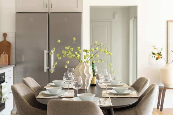 A dining table set with white plates, bowls, and wine glasses, surrounded by beige chairs.