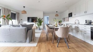 A modern kitchen with white cabinets, a dining table with chairs, and a TV mounted on the wall.