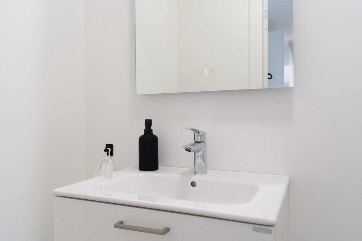 Een witte badkamer met een wastafel, een zwarte fles en een spiegel boven de wastafel.