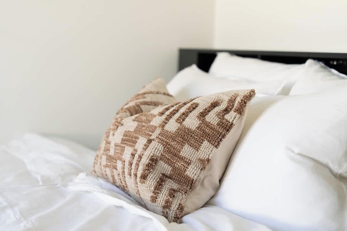 A neatly made bed with white linens and a patterned pillow.