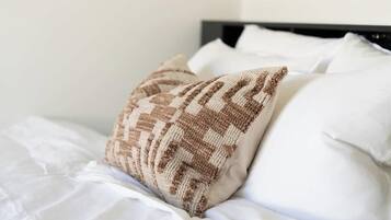 A neatly made bed with white linens and a patterned pillow.