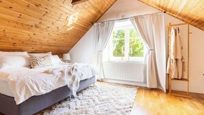 A cozy bedroom with a sloped ceiling, a bed with white bedding, a window with curtains, and a radiator. - Fully Equipped Apartment Close to Malmo Copenhagen (Vellinge)