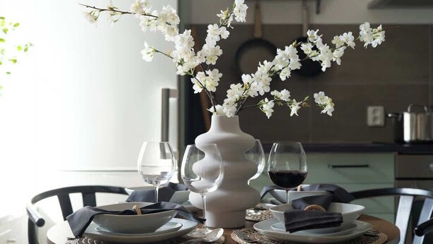 A dining table with white flowers in a vase, two wine glasses, and plates set for a meal. - Fully Equipped Apartment Close to Malmo Copenhagen (Vellinge)