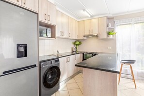 Une cuisine moderne équipée d’un réfrigérateur en acier inoxydable, d’un lave-linge encastré et d’un tabouret de bar.