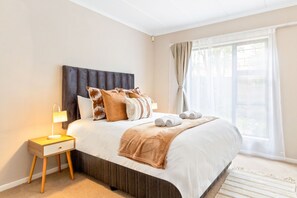 Un lit bien fait, avec une tête de lit, une lampe de chevet et une fenêtre avec des rideaux.