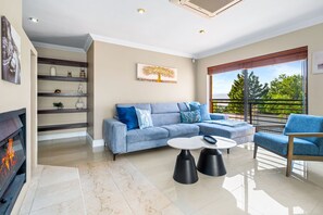A modern living room with a sofa, coffee table, and chair, a fireplace, and a balcony with a view.