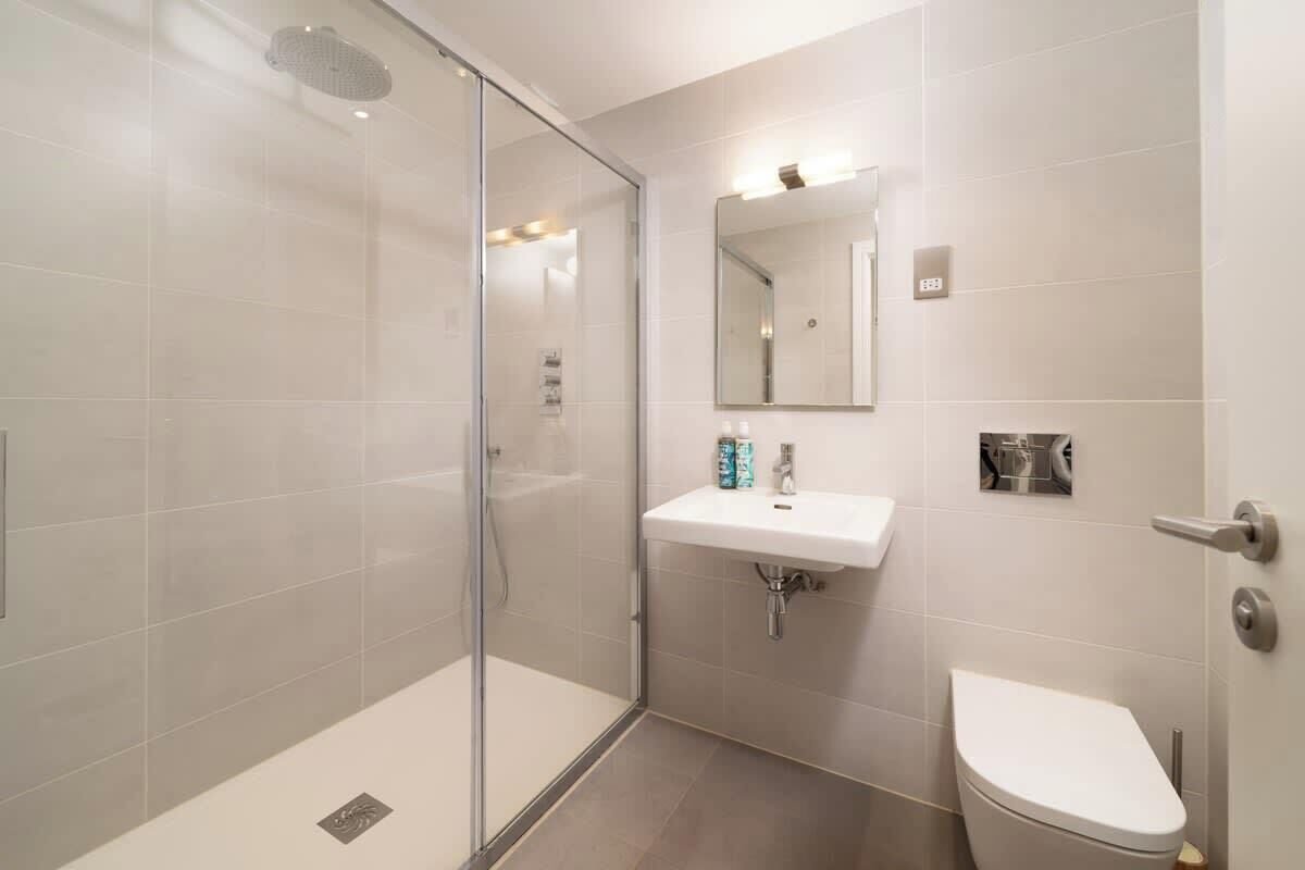 A modern bathroom with a glass-enclosed shower, a white sink, and a toilet.