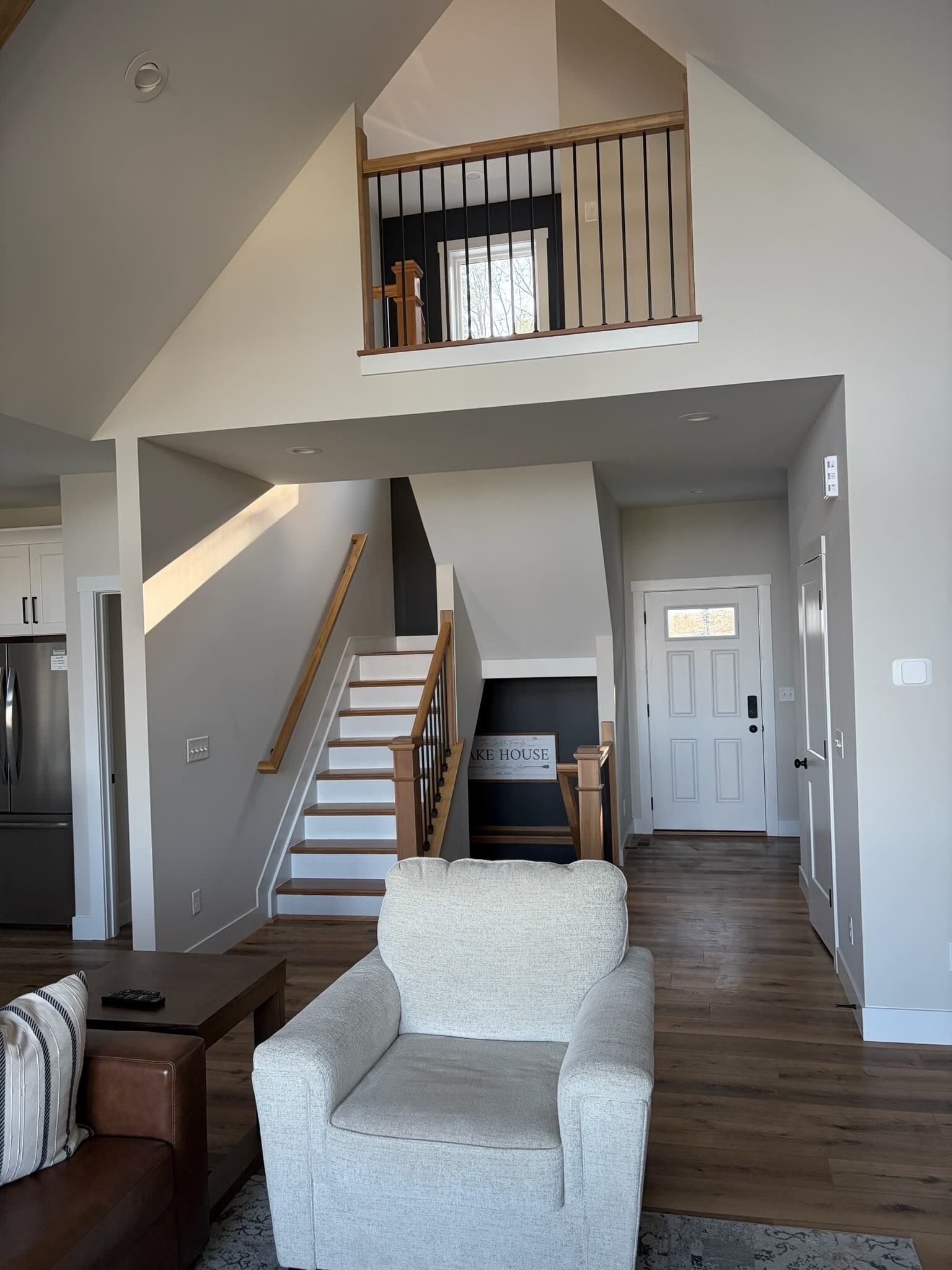 Un vaste espace de vie doté d’un haut plafond, d’un escalier menant à une mezzanine, et une cuisine visible au fond.