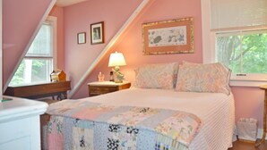 A bedroom with a sloped ceiling, a bed with floral bedding, a nightstand with a lamp, and a window with blinds.