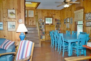 A wooden interior with a dining table and chairs, a staircase, and bookshelves.