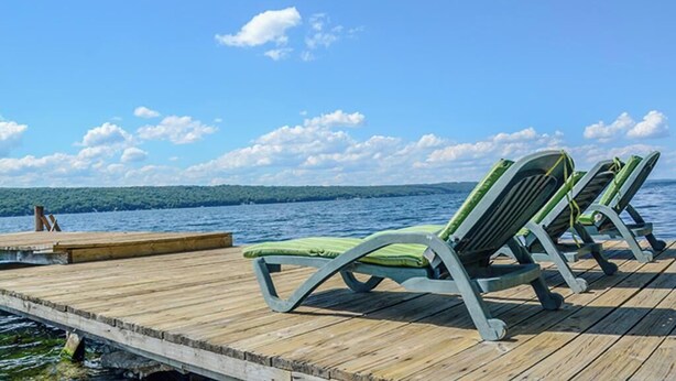A wooden dock with green lounge chairs facing a body of water.