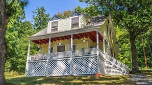 A two-story house with a porch, surrounded by trees.