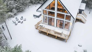 A modern cabin with a large deck, surrounded by snow-covered trees.