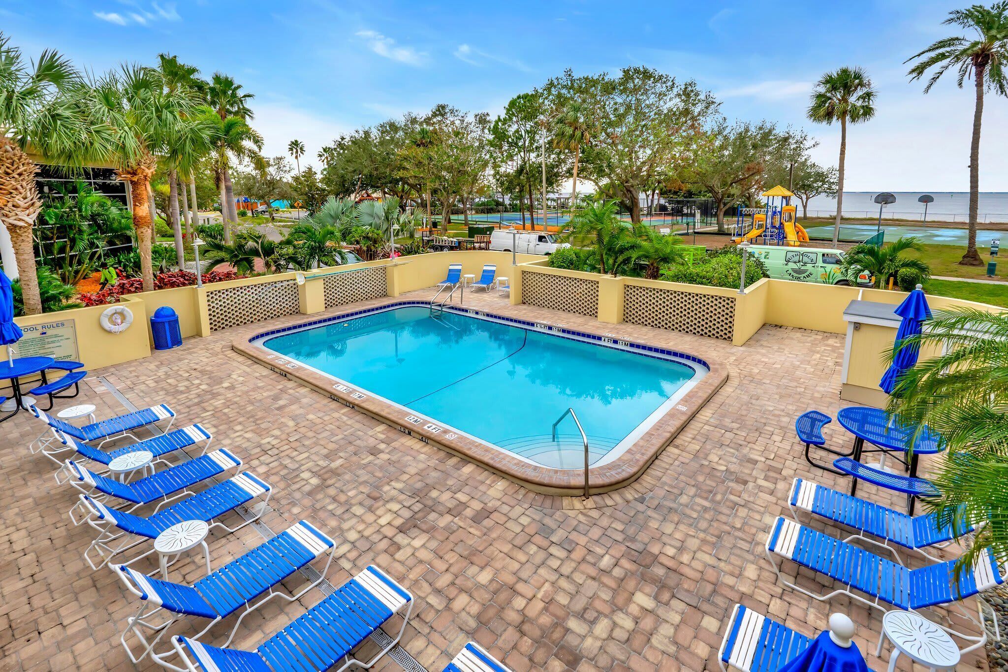 A swimming pool with blue lounge chairs and a brick patio.