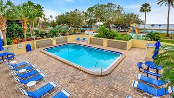 A swimming pool with blue lounge chairs and a brick patio.