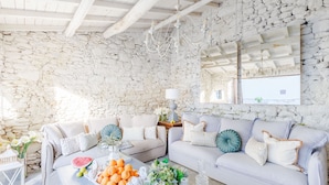 A cozy living room with stone walls, a white sofa, and a coffee table with fruits and flowers.