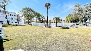 A grassy area with a white fence, trees, and a building under construction. - #1 "The village" great Studio (North Myrtle Beach)