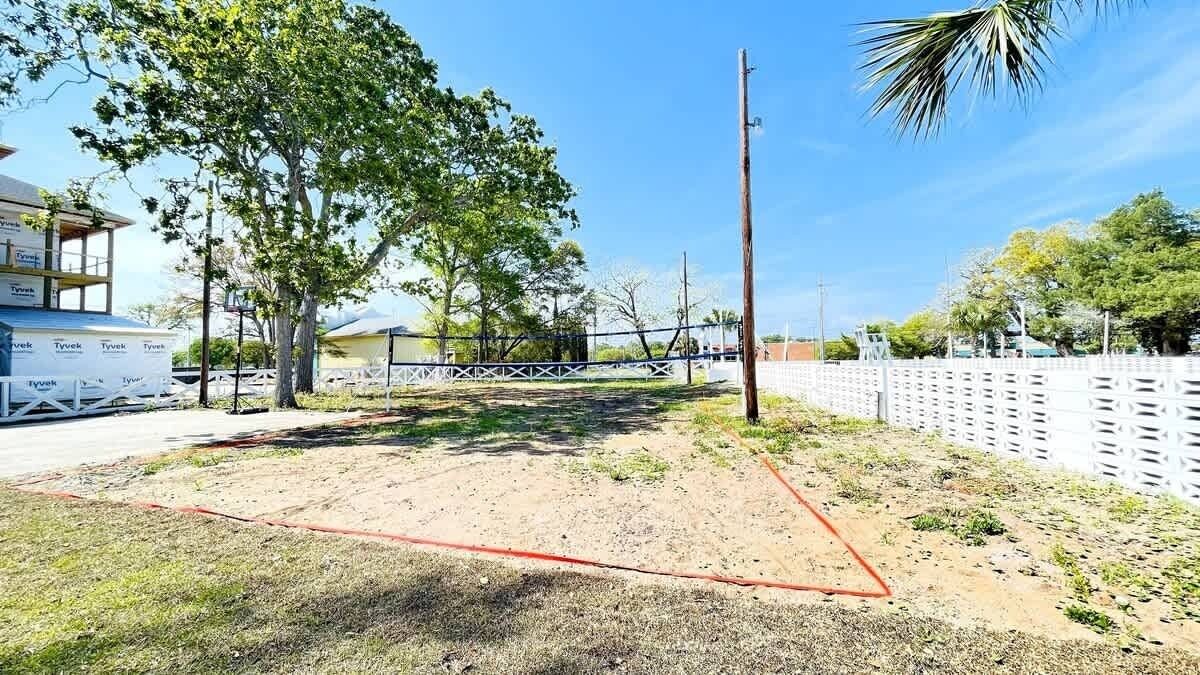 A fenced outdoor area with a dirt ground, trees, and a white fence.
