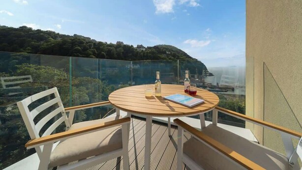 Un balcon avec une table ronde en bois, des chaises blanches et une rambarde en verre.