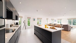 Une cuisine moderne dotée d’un grand îlot central, de meubles de rangement aux couleurs sombres et offrant une vue sur l’espace de vie.