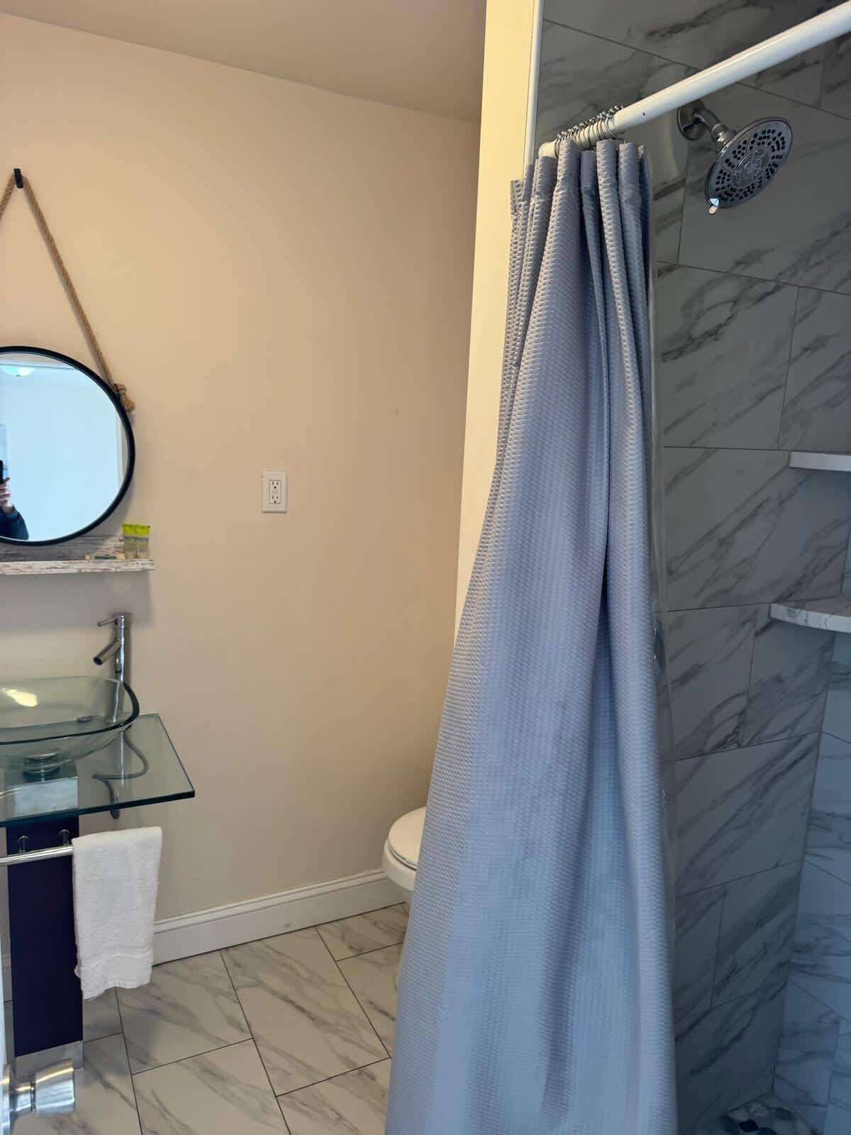 A bathroom with a glass sink, a round mirror, a toilet, and a shower curtain.
