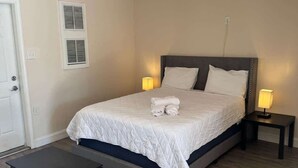 Un dormitorio con cama, lámparas de noche, una mesita y una puerta.