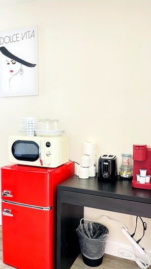 Eine KĂŒchenzeile mit einem roten KĂŒhlschrank, einer Mikrowelle, einer Kaffeemaschine und einem MĂŒlleimer.