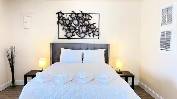 A hotel room with a bed, two bedside tables, a wall-mounted artwork, and a window with blinds.