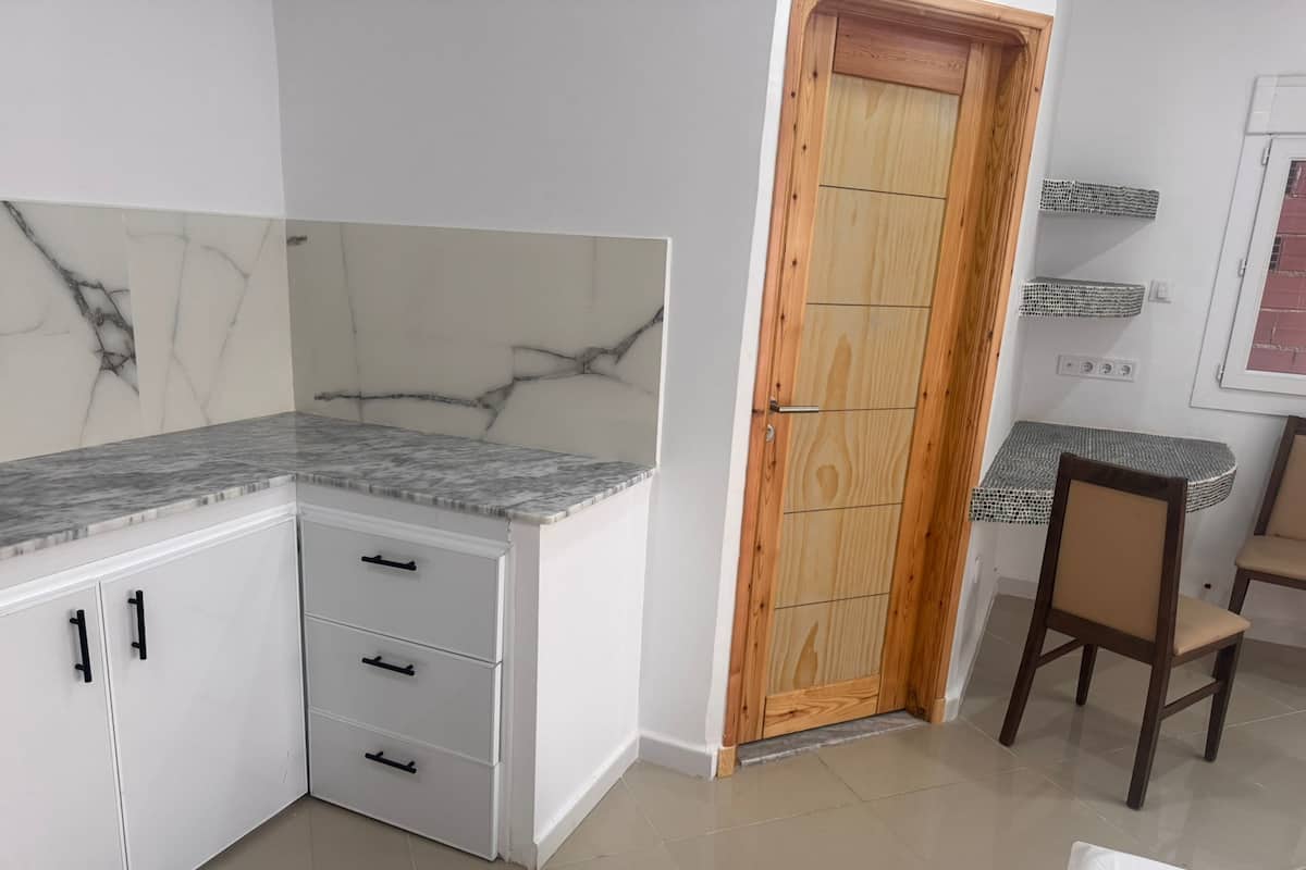 Una cocina con armarios blancos, encimera de mármol y puerta de madera.