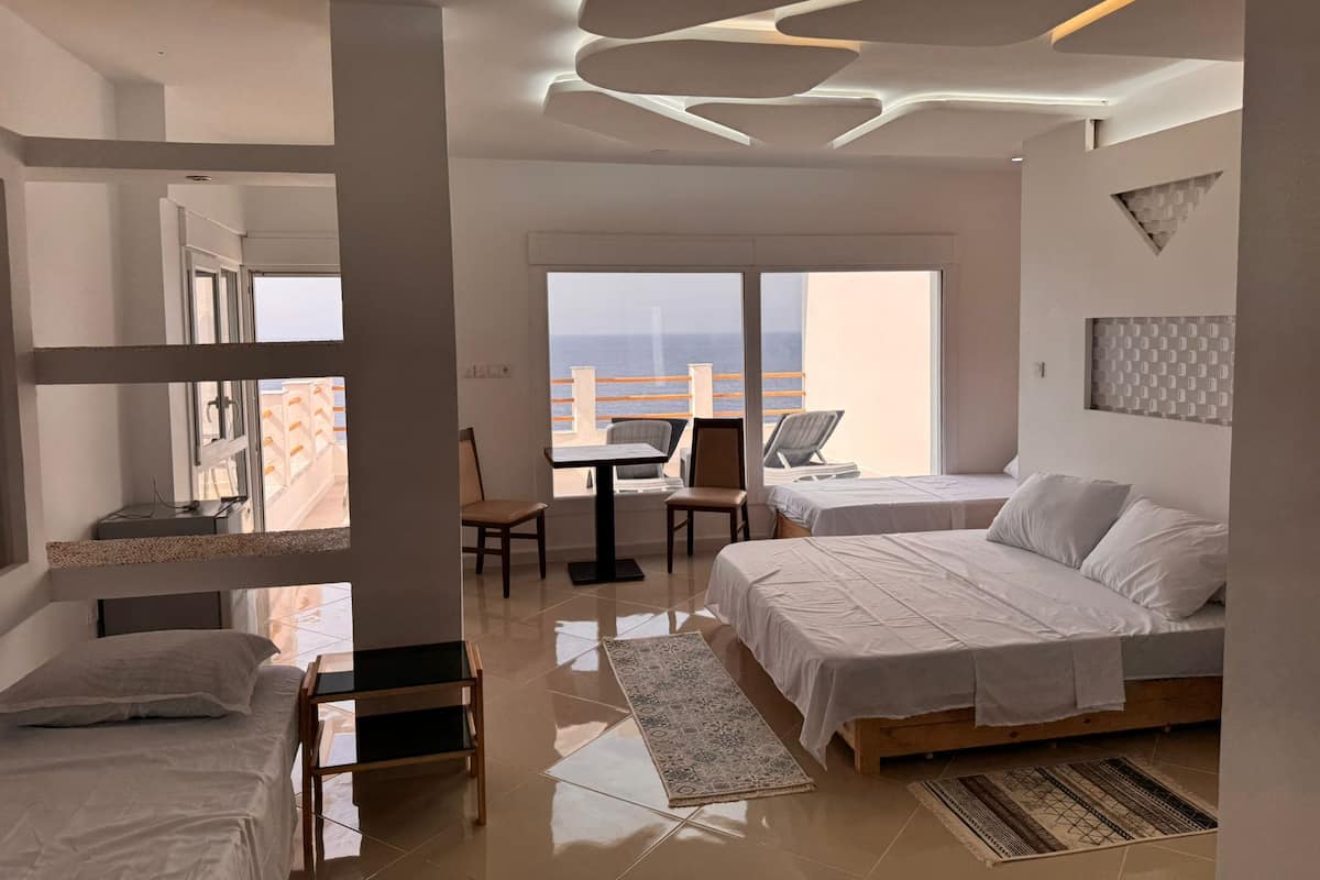 Una habitación de hotel moderna con balcón, dos camas, escritorio y vista al océano.