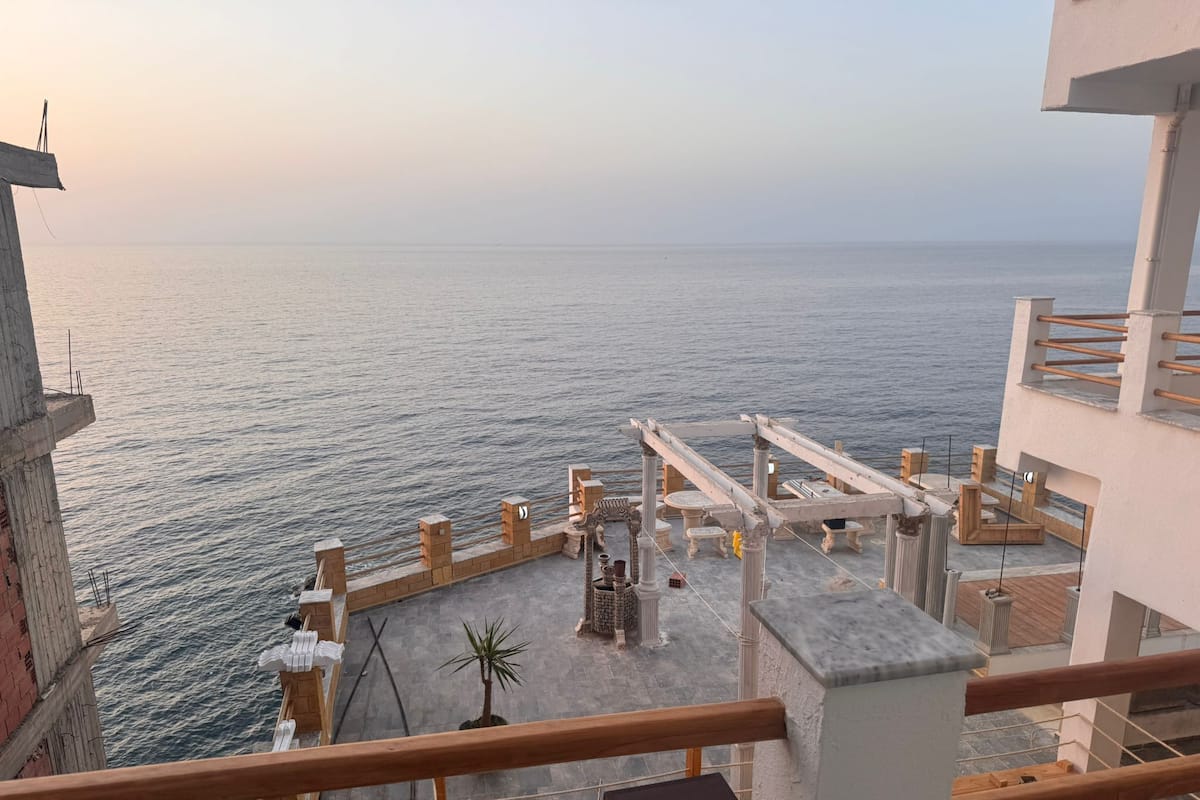 Una terraza con vista al mar, que incluye una cubierta de madera, columnas de piedra y un área de estar.