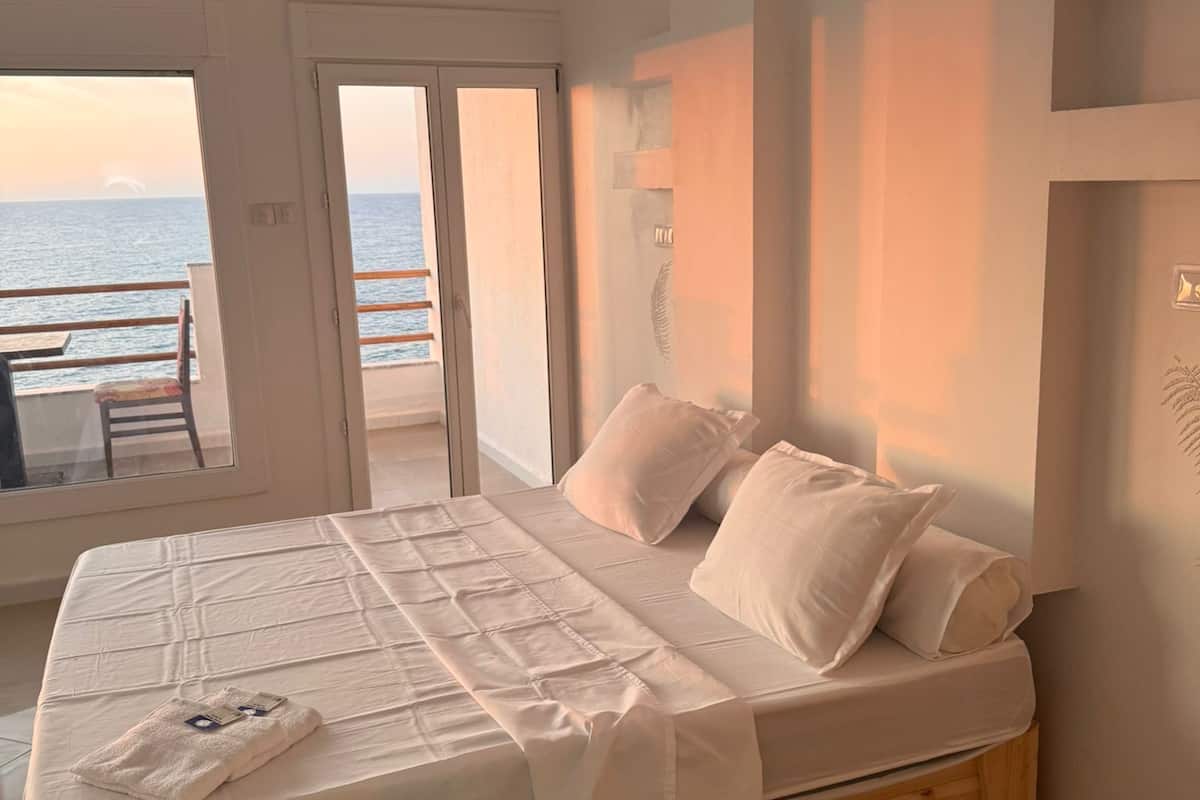 Un dormitorio con una cama grande, vistas al mar a través de una puerta abierta y un balcón con una silla.