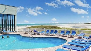 A pool area with lounge chairs and a view of the beach.