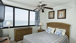 A bedroom with a bed, a nightstand, a dresser, a ceiling fan, and a window with curtains.