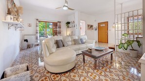 Una sala de estar con un sofá seccional, una mesa de centro, piso estampado, un ventilador de techo y vistas a través de una ventana.