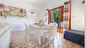 Una habitación con una mesa de comedor, sillas, un banco, un ventilador de techo y vistas a un espacio exterior a través de un ventanal.