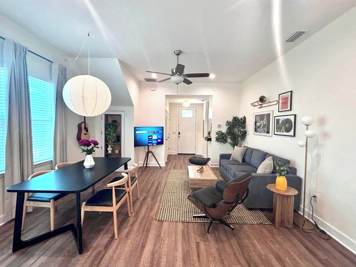 Un salon moderne comprenant un coin repas, un ensemble de canapés, un téléviseur et un ventilateur de plafond.