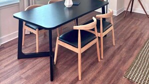 Un coin repas avec une table sombre, des chaises en bois, un luminaire suspendu et une guitare accrochée au mur.