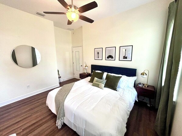 Quarto com cama, ventilador de teto, espelho e quadros nas paredes.