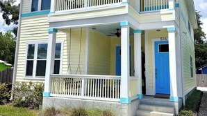 Une maison à deux étages avec un balcon au deuxième étage, un porche à l’avant et une porte bleue.