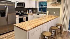 Une cuisine moderne dotée d’appareils électroménagers en acier inoxydable, d’un îlot central en bois avec des tabourets et d’un éclairage suspendu.