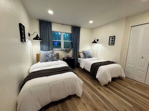 A bedroom with two beds, a window with curtains, a bedside table, a lamp, and a wardrobe. - Magnolia Modern, Near UF, Shands, Private (Gainesville)