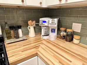 Une cuisine équipée d’une machine à café, de pots à épices et d’un plan de travail en bois.