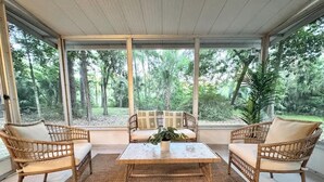 Une véranda meublée de mobilier en osier, avec une table centrale et une vue sur une forêt.