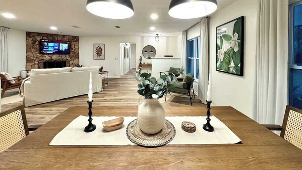 Un coin repas avec une table en bois, deux bougies, un vase contenant des feuilles vertes et un set de table en fibres tressées.